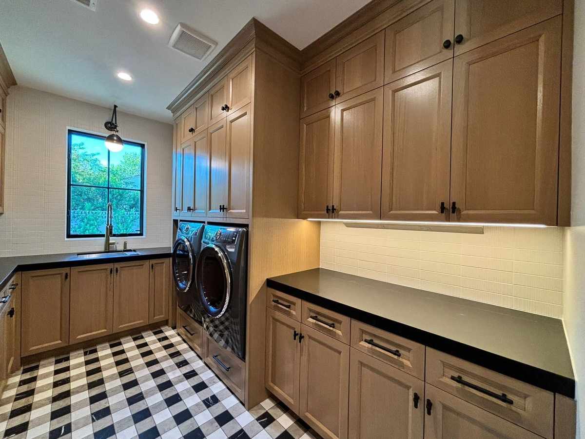Custom laundry room cabinetry with black countertops and checkered marble tile floor in South Florida