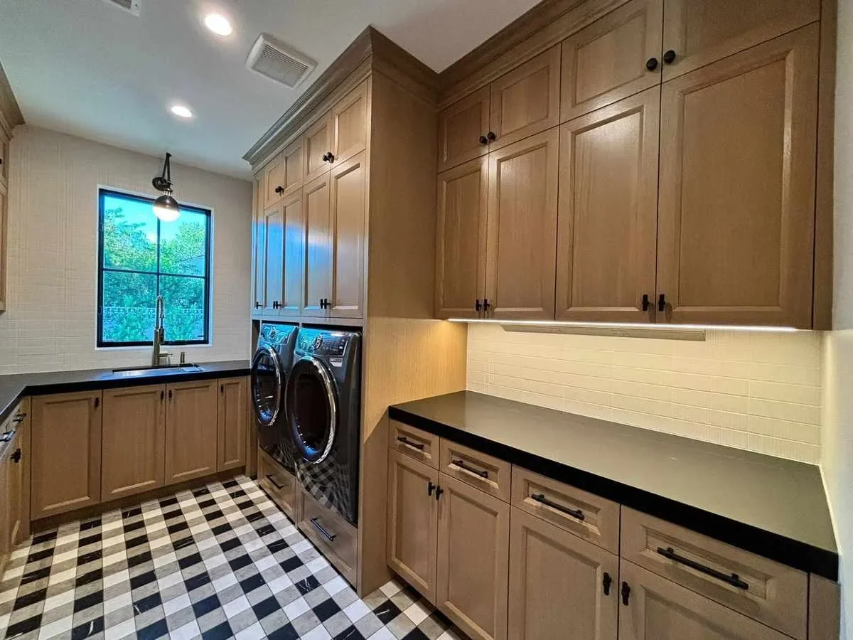 Custom laundry room cabinetry with black countertops and checkered marble tile floor in South Florida