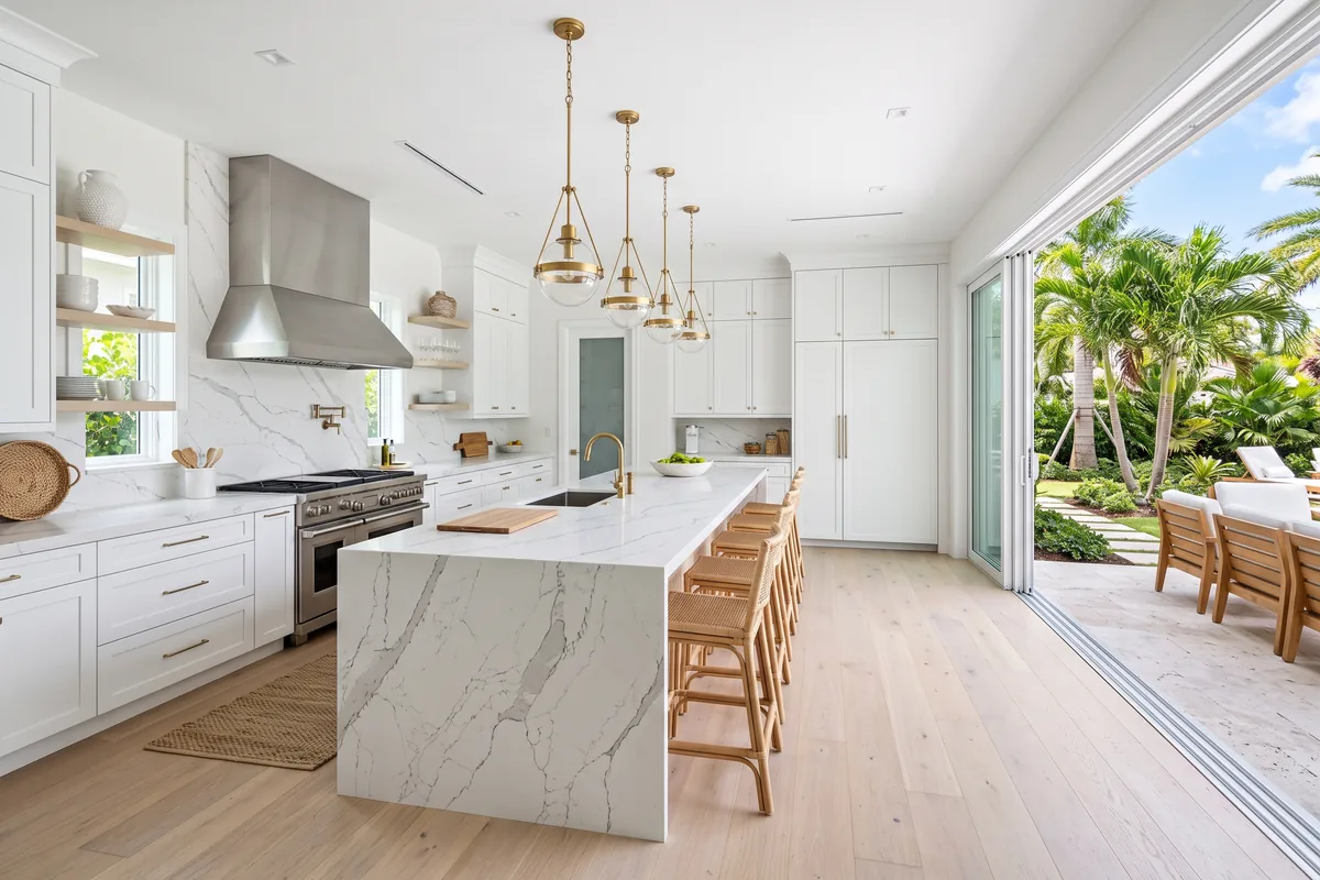 Panoramic open-plan Palm Beach County kitchen with a long quartz island and brass pendant lights